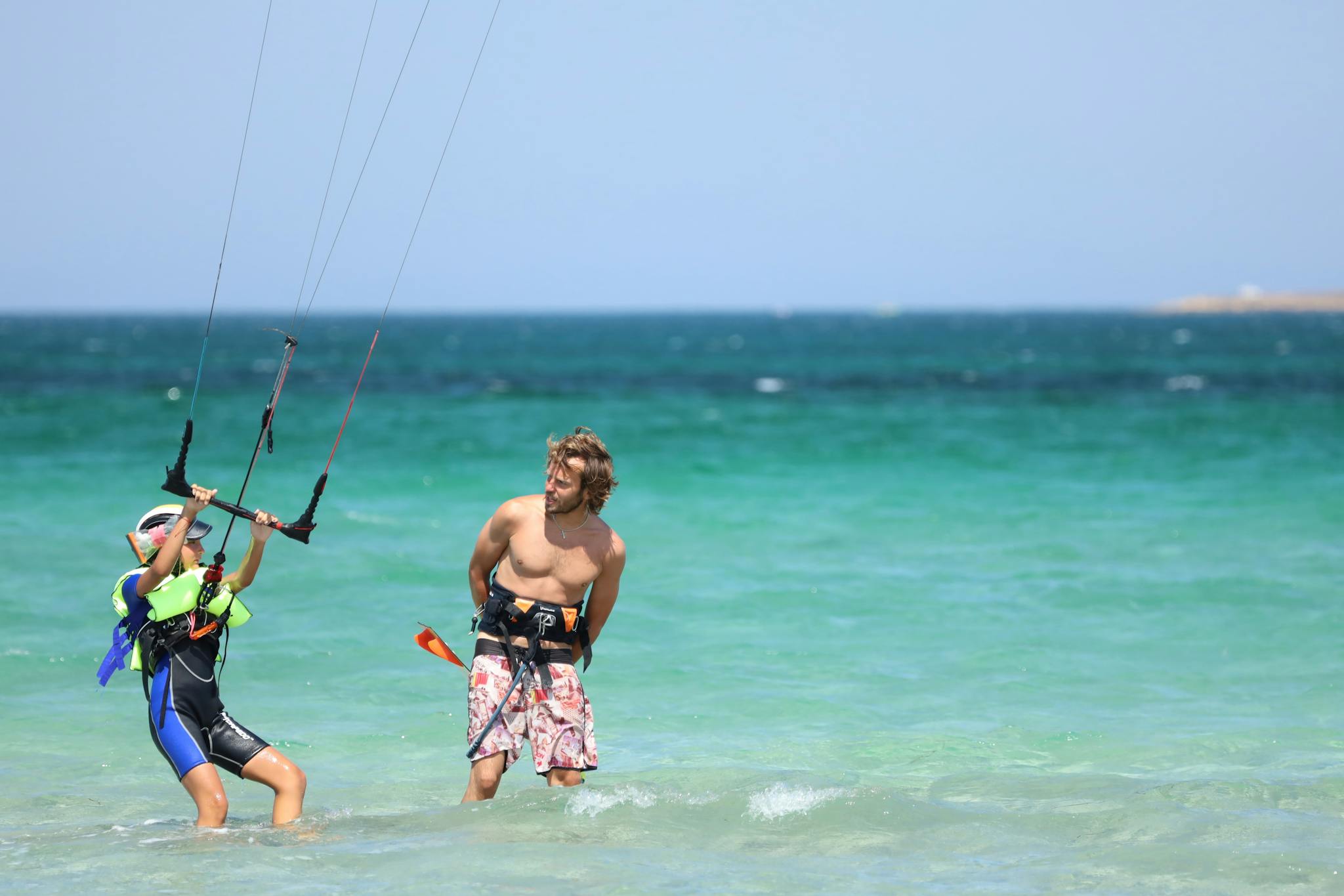 A kite surfing lesson with an instructor helping a student in the vibrant blue sea.