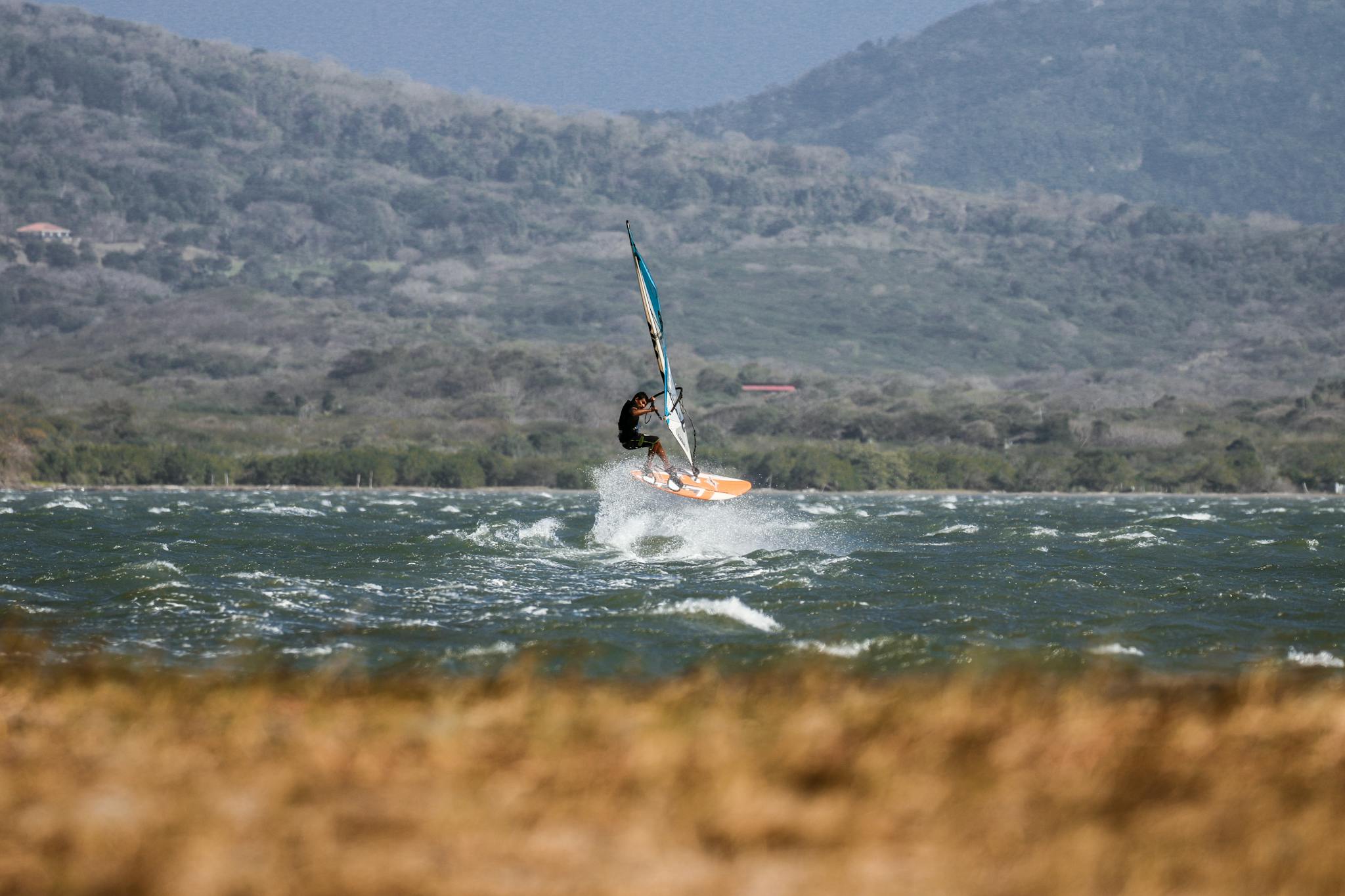 Action-packed windsurfing on a lake surrounded by mountains. Perfect for sports enthusiasts.