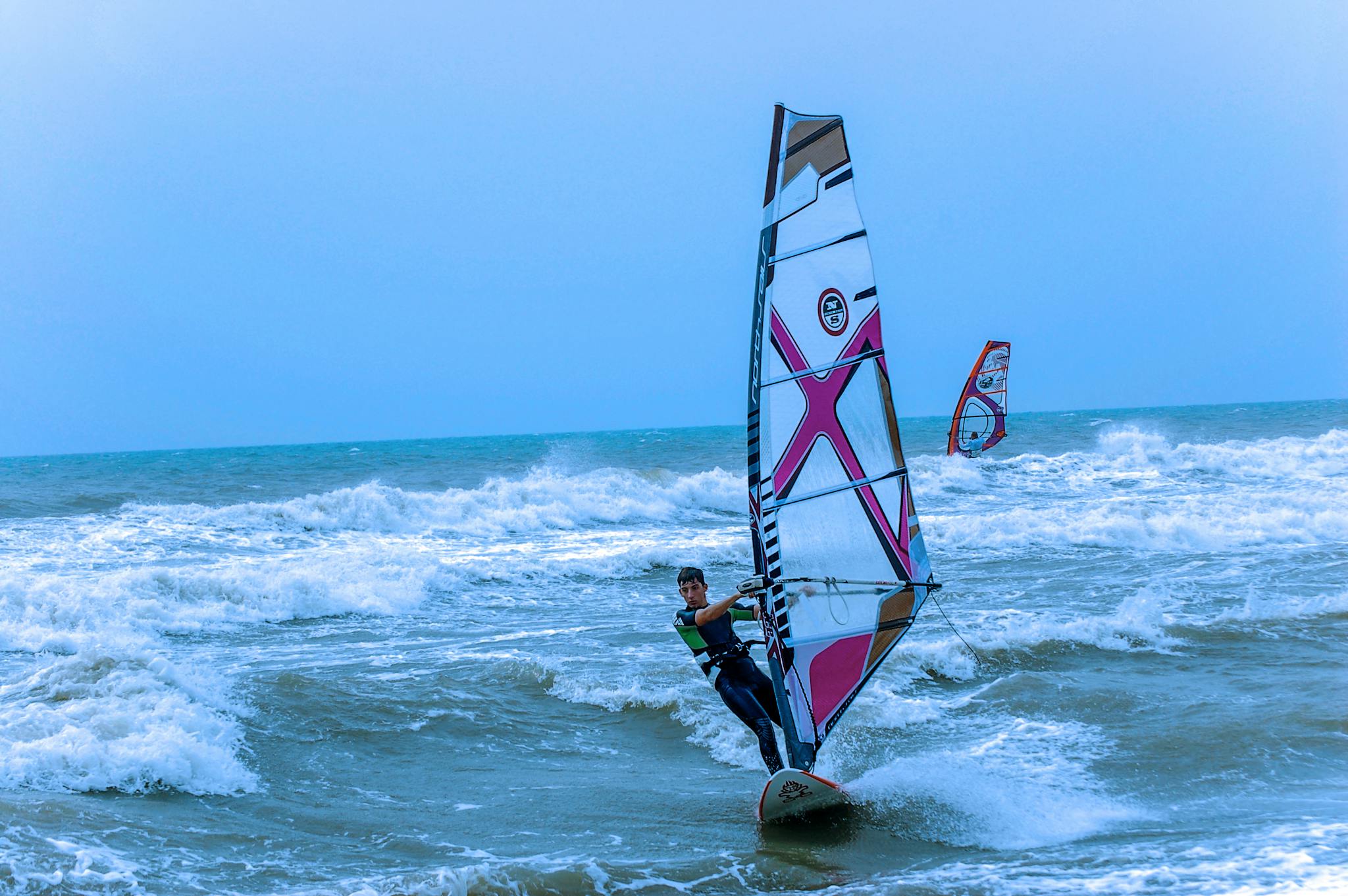 An adventurous man windsurfing skillfully over the ocean waves on a windy day.