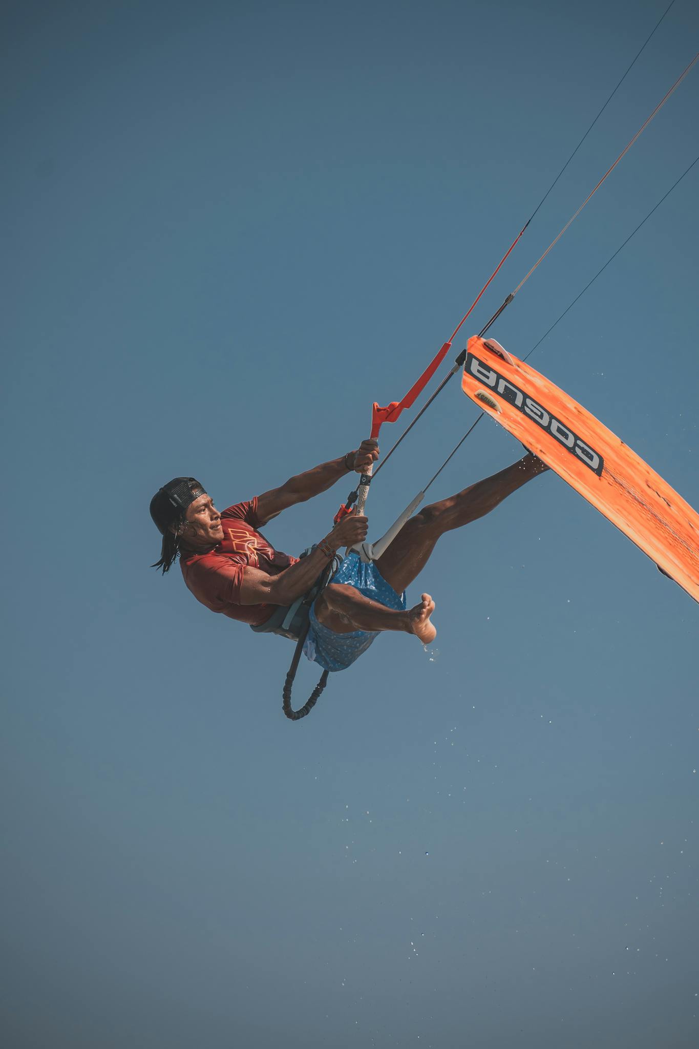 An athlete performs an impressive kiteboarding trick midair against a vibrant blue sky, showcasing extreme sports mastery.
