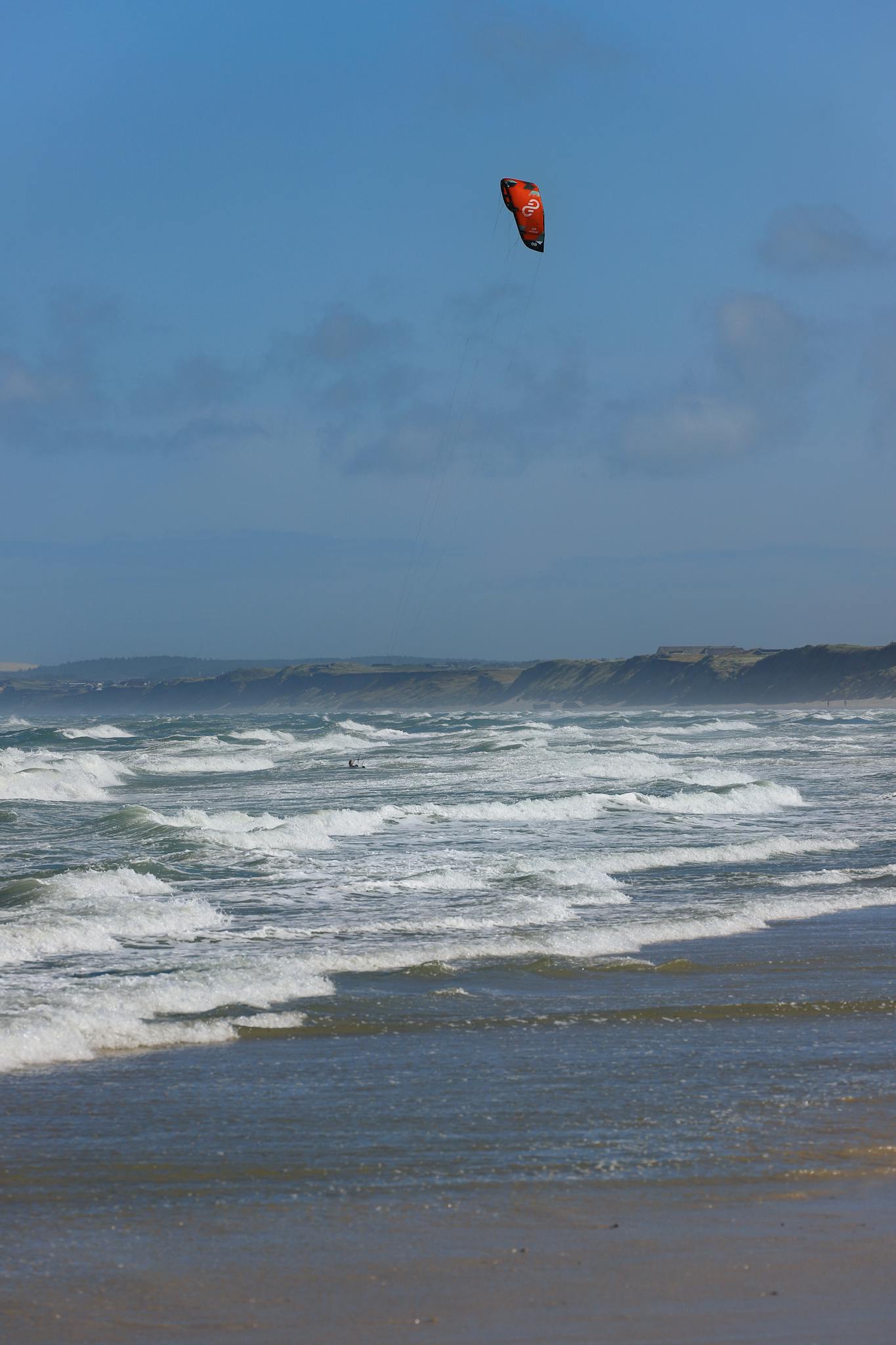 Experience thrilling kitesurfing on a windy beach in Denmark with waves and expansive sandy shore.